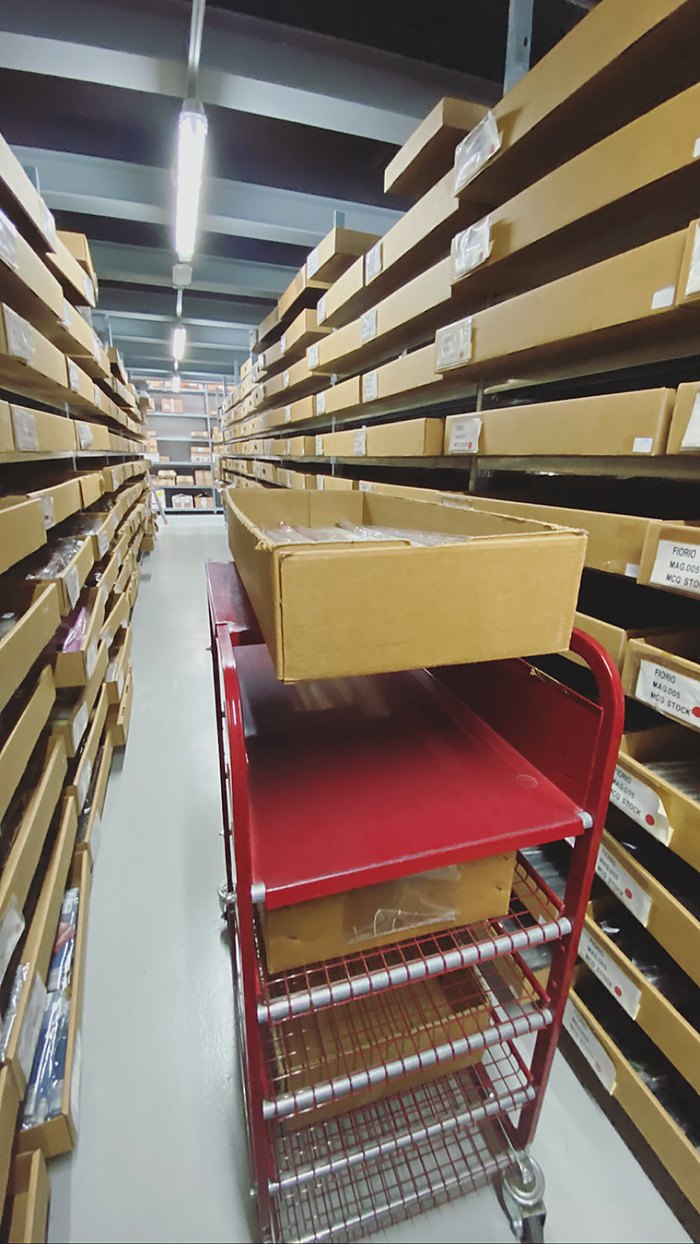 Stockroom aisle — boxed shoes on the racks, picking trolley in between