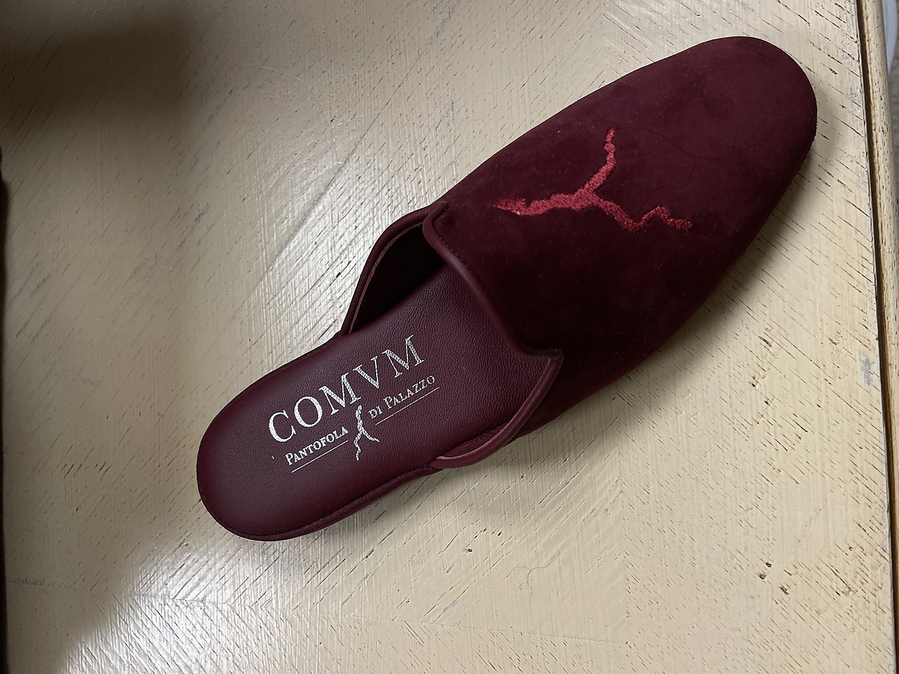 Burgundy velvet slipper with the COMVM mark on the vamp