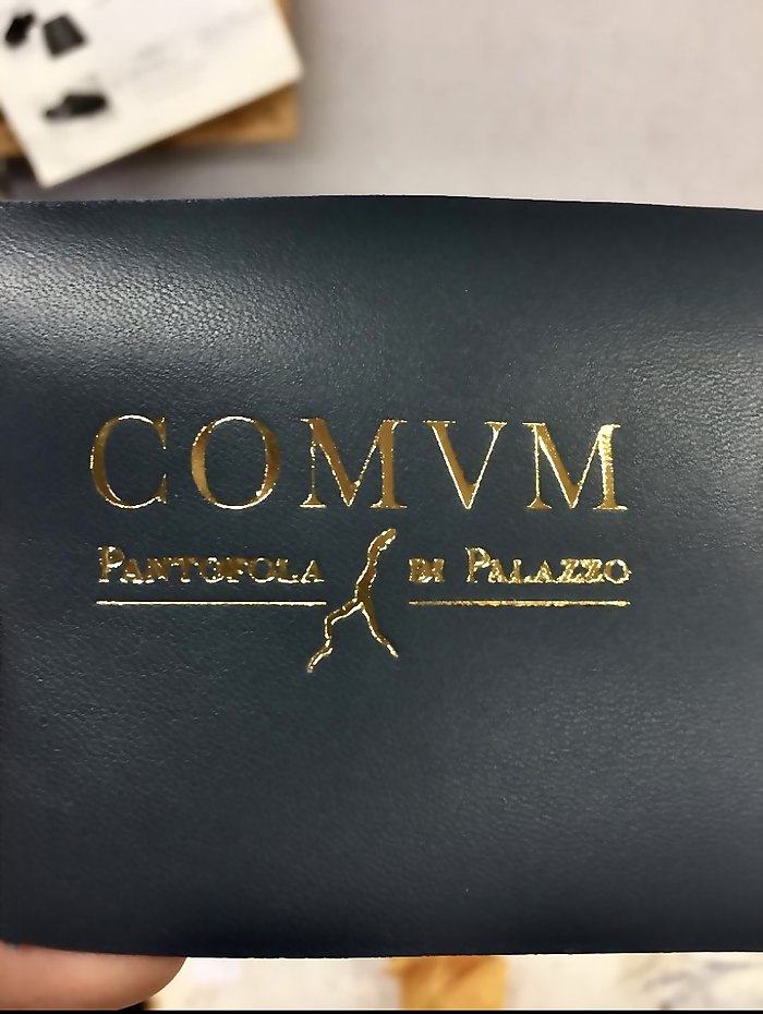 COMVM wordmark stamped in gold on black leather